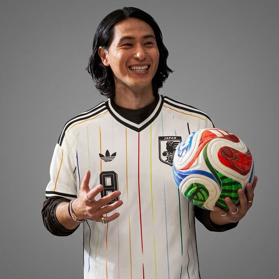 Landslagsstjernen Takumi Minamino viser frem den splitter nye Japan 2026 bortedrakten. Det dristige designet med de tynne, flerfargede vertikale stripene på den rene, hvite basen feirer den moderne "Samurai Blue"-identiteten på den største globale scenen under VM 2026.