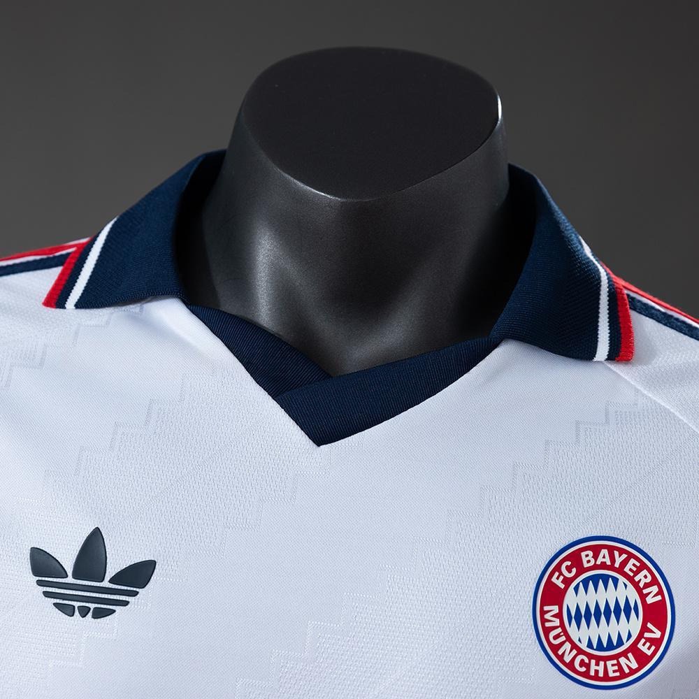 Nærbilde av marineblå krage, tonalt stoffmønster og klassisk Bayern-emblem på 26/27-bortedrakten