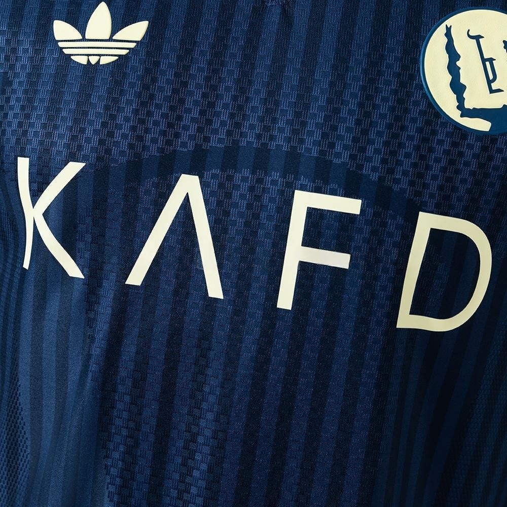 Nærbilde av tonale striper, gult klubbmerke og brystmotiv på Al-Nassr bortedrakt