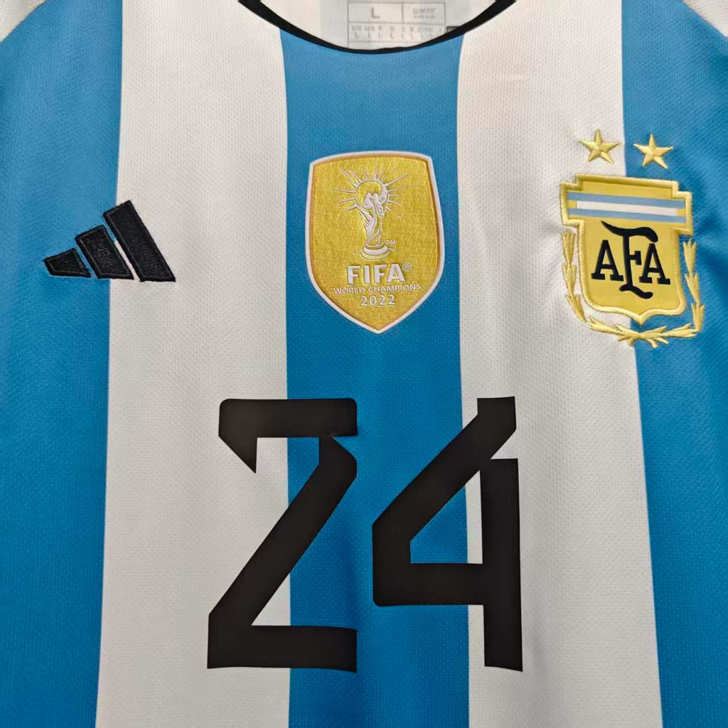 Nærbilde av gullfarget mestermerke, to stjerner og nummer 24 på Argentina retrodrakt